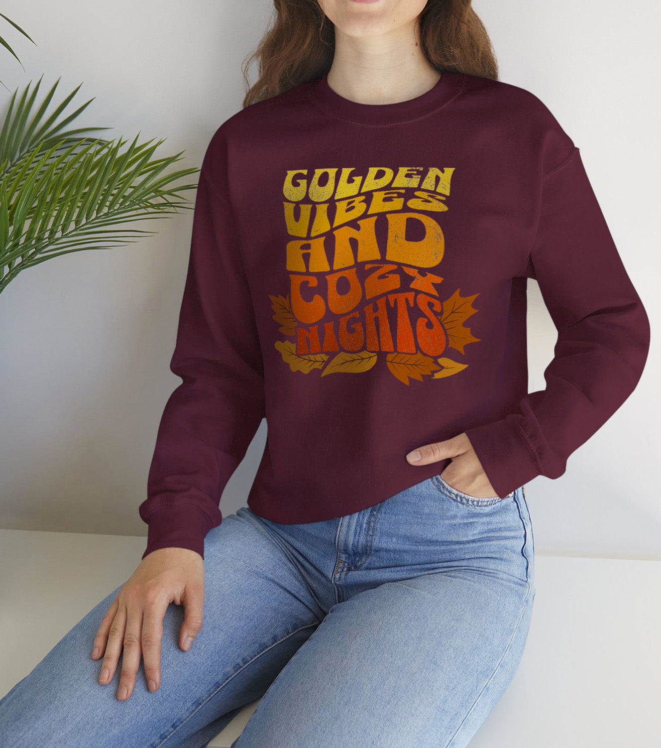 Maroon sweatshirt with “Golden Vibes and Cozy Nights” text in yellow-to-orange gradient and autumn leafs worn by a fall vibes fan BimBangDesign