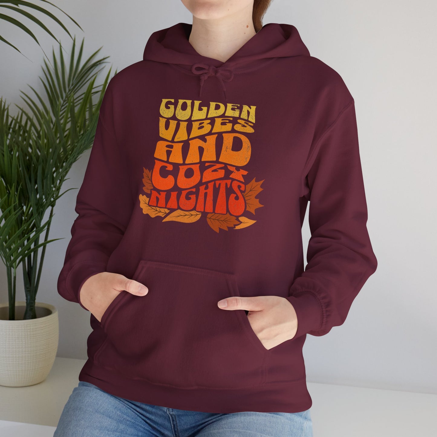 “Golden Vibes and Cozy Nights” hoodie with a text print in yellow-to-orange gradient and autumn leafs worn by a comfy season lover BimBangDesign